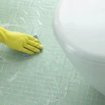 Person wearing yellow gloves applying adhesive while laying Acid Proof Full Body Porcelain Tiles in a bathroom.