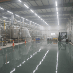 Wide factory interior with shiny floors from acid resistant flooring installation, stainless steel tanks on the left, a forklift on the right, and bright overhead fluorescent lights.